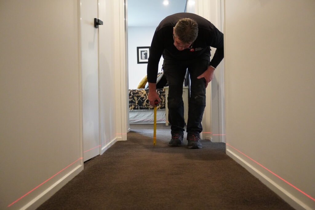 Inspector using a floor level tool to detect uneven flooring or structural issues.
